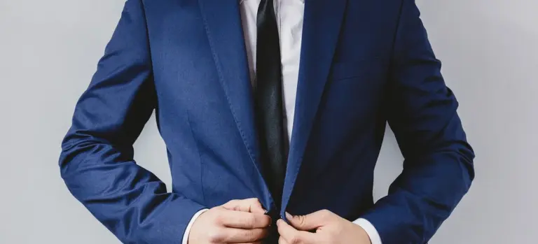 Person in a navy blue suit adjusting the jacket, wearing a white shirt and black tie.