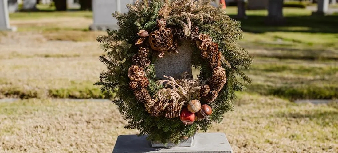 Wreath placed on a gravestone in a cemetery, with dried pinecones and foliage.