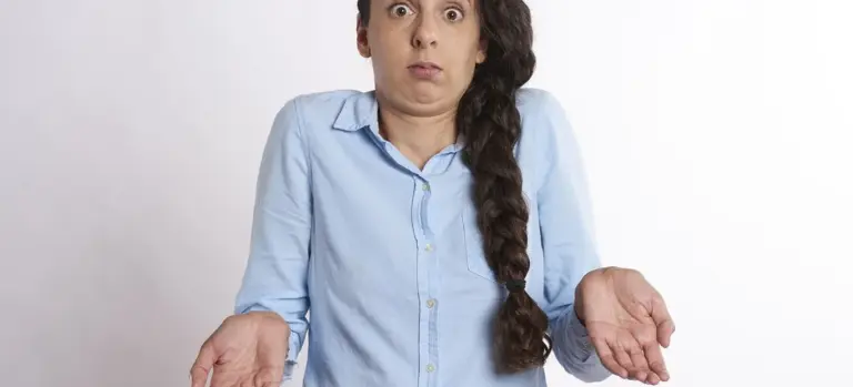 A woman in a light blue shirt with a long braid, looking puzzled while shrugging, illustrating uncertainty about wearing blue to a funeral.