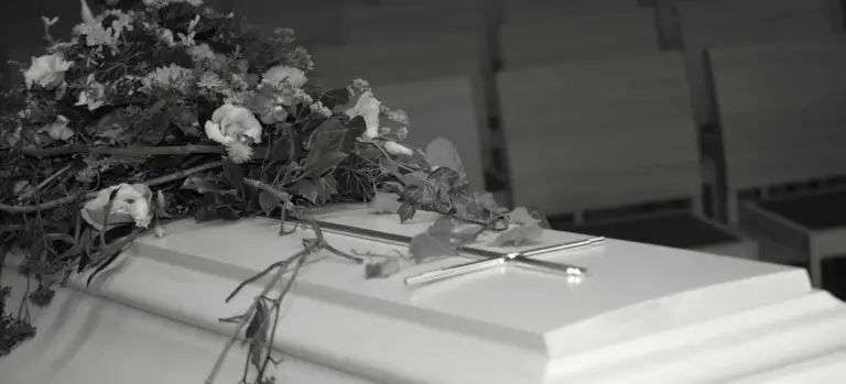 Close-up of a white funeral casket topped with a floral arrangement during a wake service.