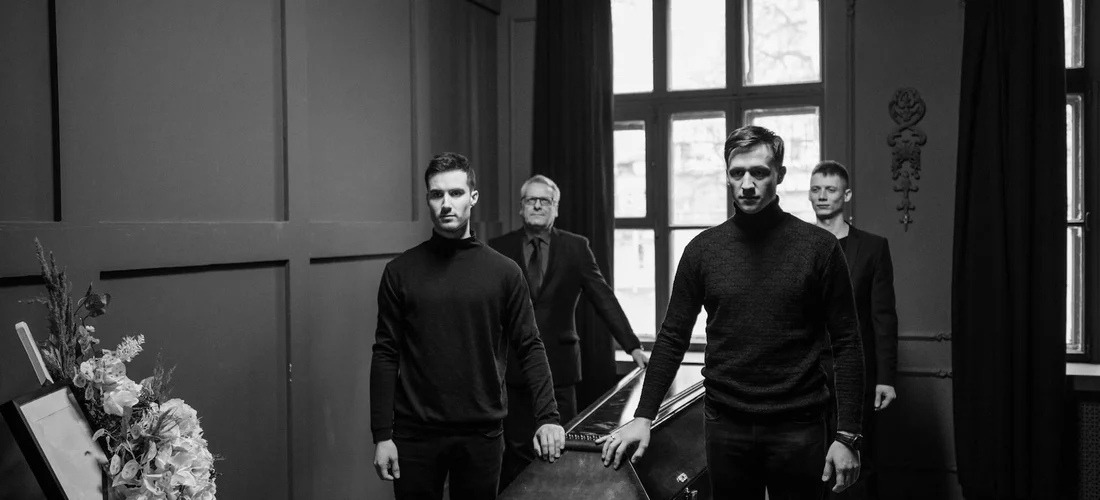 Four men dressed in black in a dim room/hallway, representing the professional path to becoming licensed in funeral services.