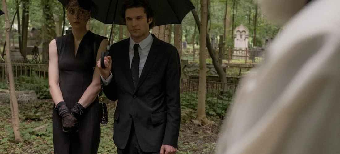 Two mourners in formal black attire standing in a cemetery under an umbrella, reflecting on funeral options.