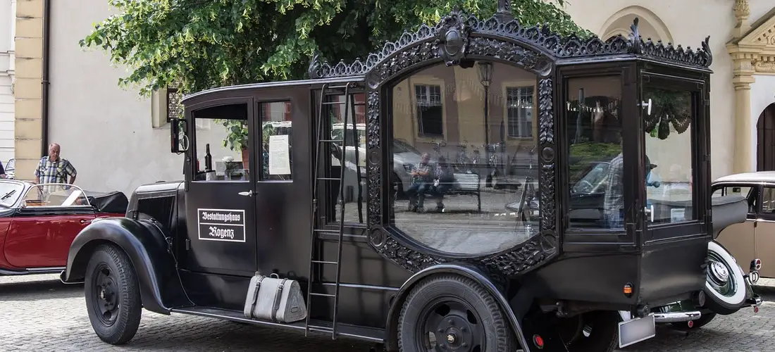 Black vintage funeral hearse with ornate windows parked on a cobblestone street