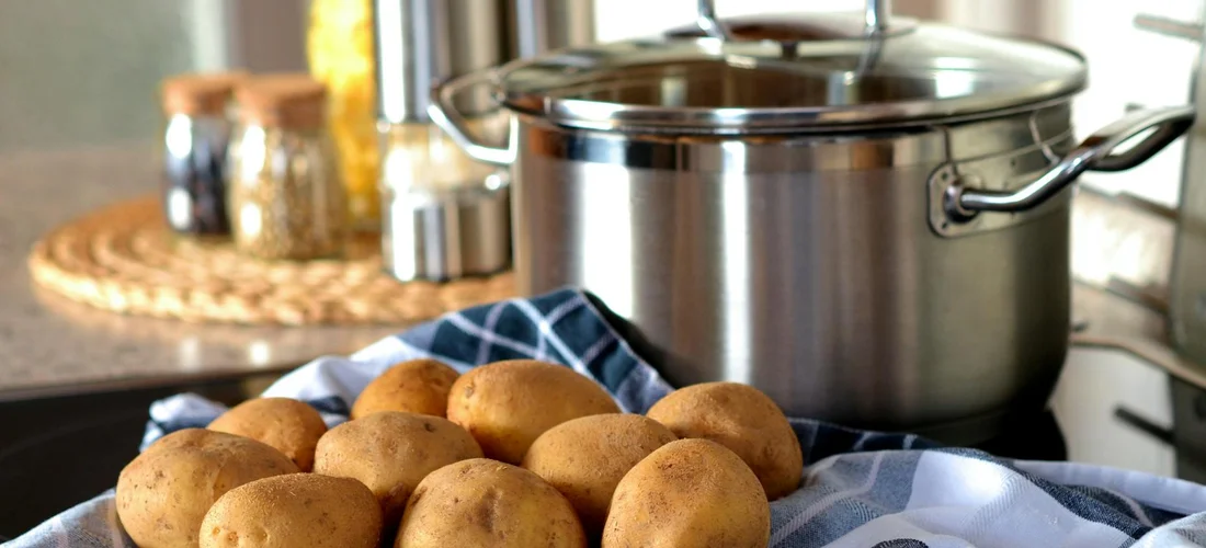 Tray of funeral potatoes resting on a blue cloth with a stainless steel pot in the kitchen background