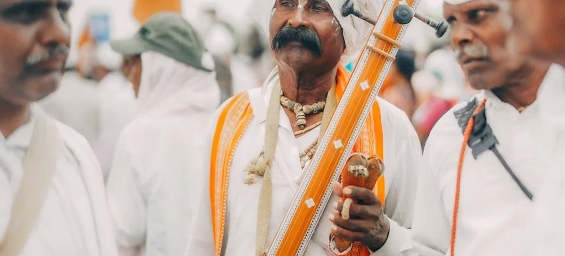 Mourners in white traditional attire in a funeral procession, with a musician playing a long-necked string instrument