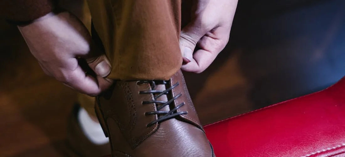 Close-up of brown leather dress shoes being laced, illustrating formal footwear choices for funerals.