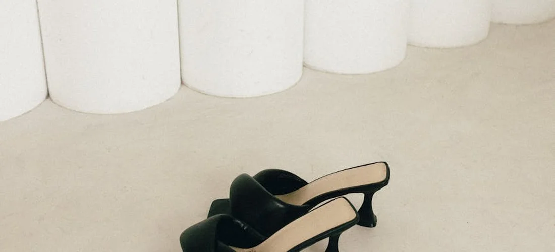 Two black high-heeled shoes with straps resting on a light, neutral floor.
