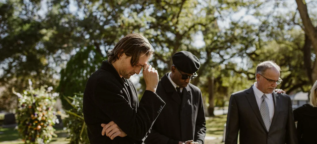 Mourners dressed in dark, modest clothing at an outdoor spring funeral.