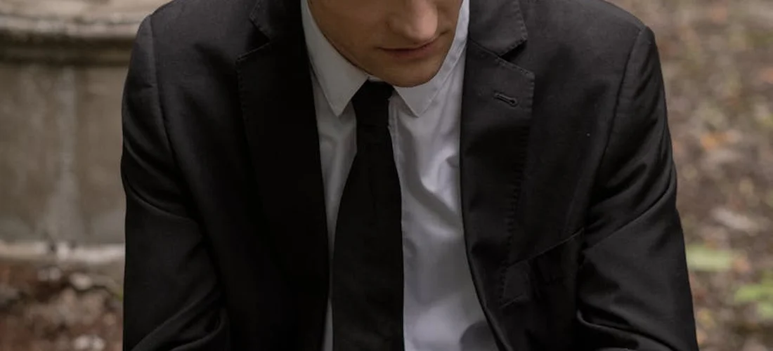 Person wearing a dark suit with a white shirt and black tie, appropriate for a funeral viewing.
