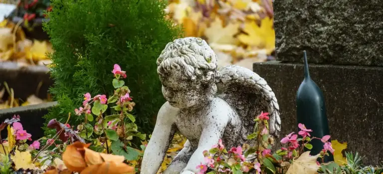 Stone angel statue amid greenery and autumn leaves in a memorial garden