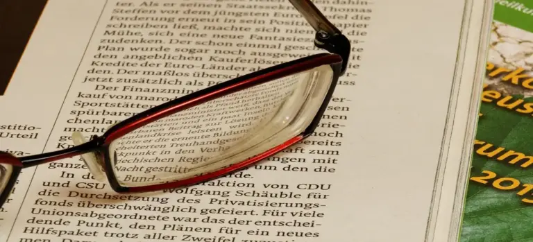 A pair of reading glasses resting on a newspaper with German text.