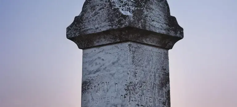 Weathered stone monument against a soft, pale evening sky.