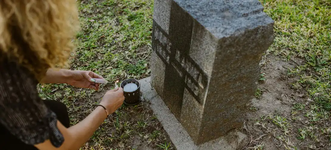 A person kneels at a grave, placing a coin on the headstone in a cemetery