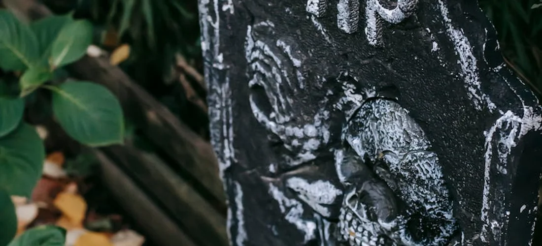 Close-up of a weathered gravestone with carved details, surrounded by green foliage.
