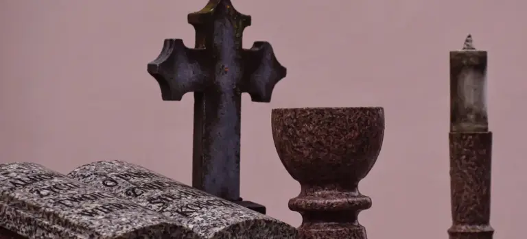 Old gravestones and a cross-shaped headstone in a cemetery