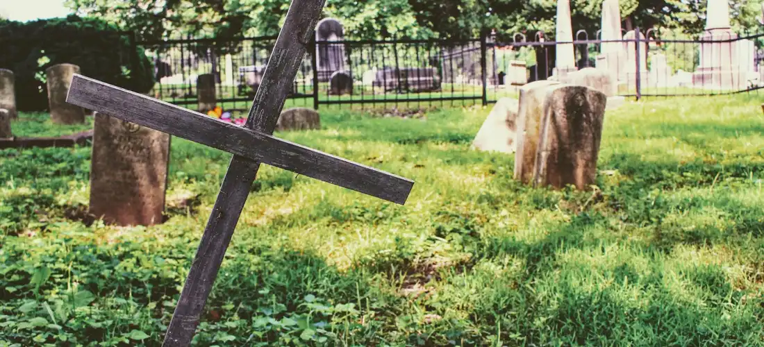 Slanted wooden cross in a cemetery with tombstones and green grass