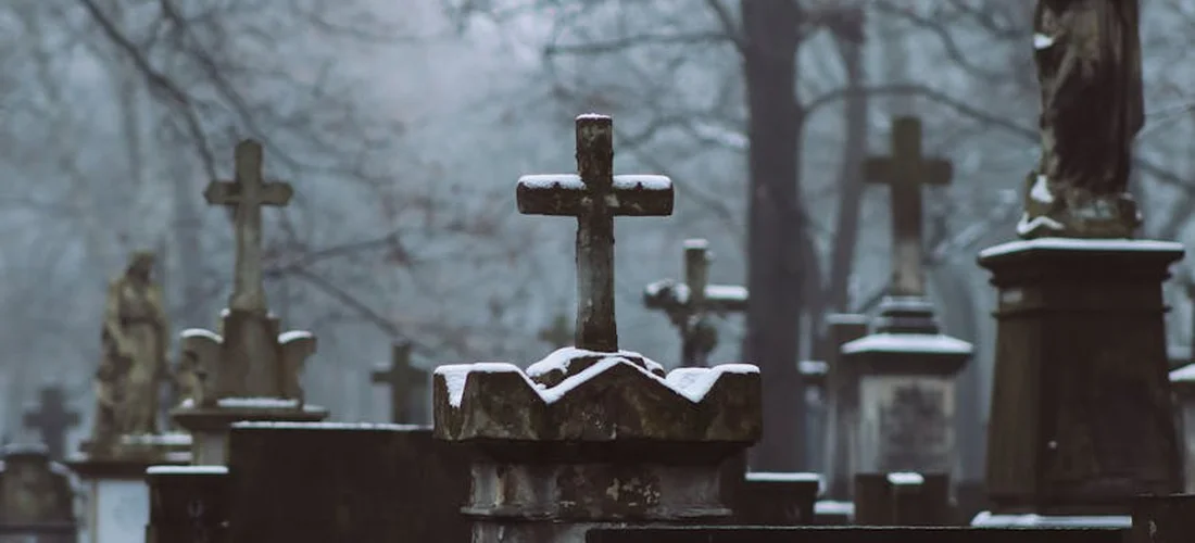 Rows of weathered gravestones with crosses in a cemetery, illustrating death, funeral costs, and how policy riders can adjust a life insurance benefit.