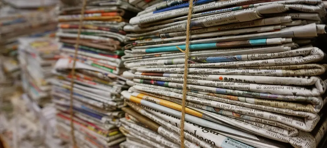 A close-up of stacked folded newspapers tied with a string, illustrating archival sources for local obituaries.