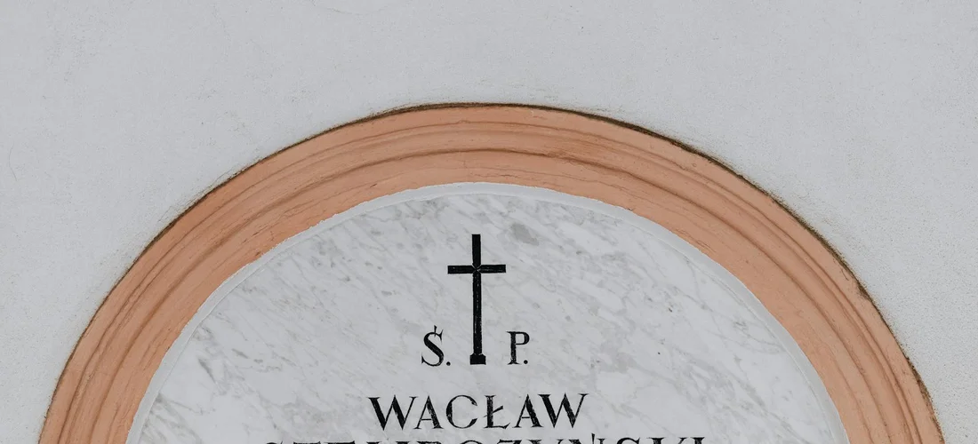 Circular marble memorial plaque with a cross at the top and the name Wacław engraved below.