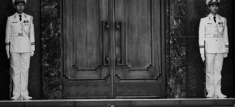 Two military honor guards stand at attention on either side of a large wooden doorway.