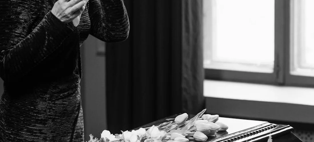 A civilian guest in dark clothing stands near a casket adorned with flowers at a military funeral.