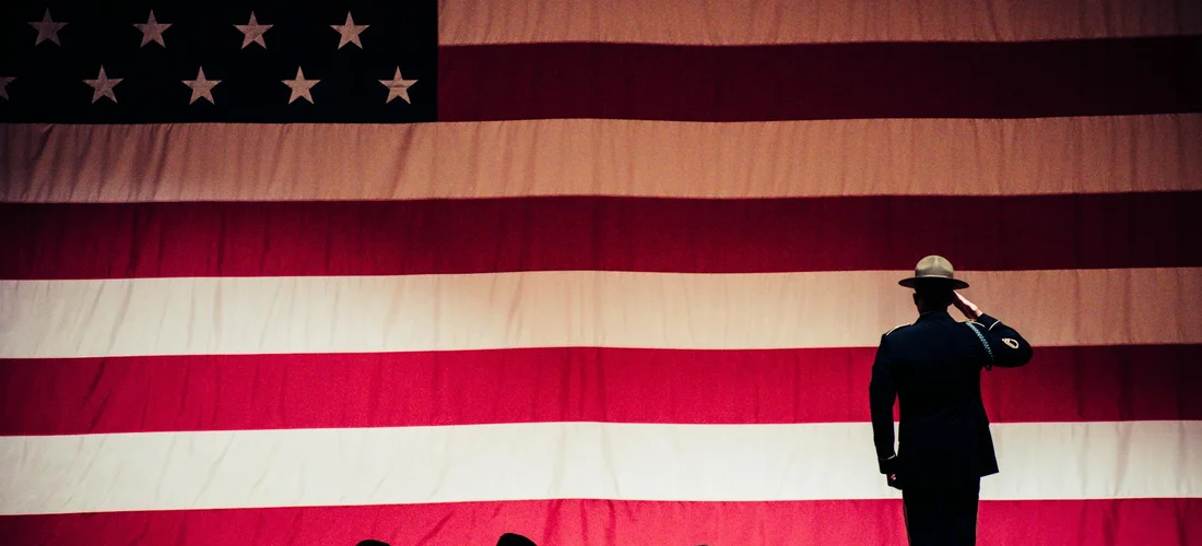 A uniformed service member saluting in front of a large American flag, symbolizing military funeral rituals.