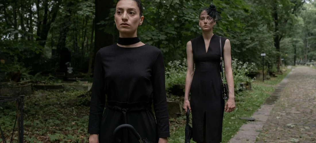Two people in modest, black outfits walking along a park path in a somber setting, illustrating funeral attire.