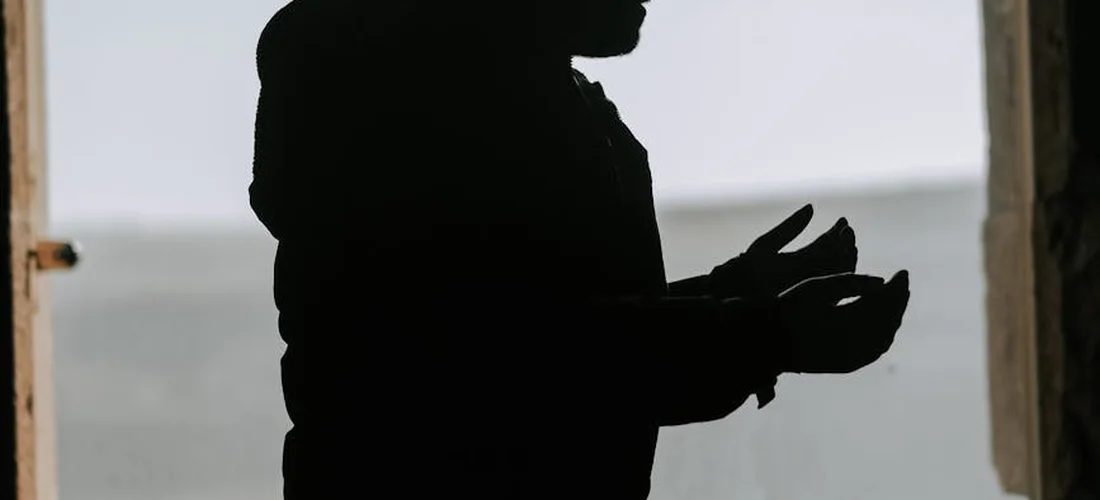 Profile silhouette of a person with hands raised in supplication