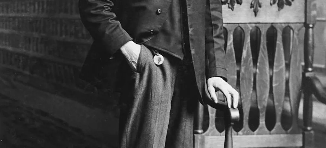 Black-and-white photo of a man in a navy suit with a pocket watch, standing by a railing.