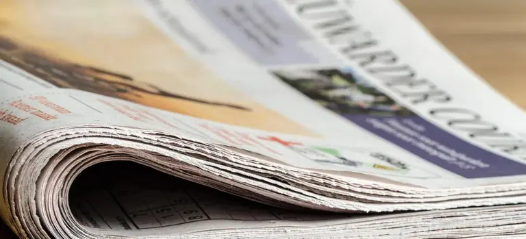 A stack of folded newspapers, representing traditional print obituary notices.