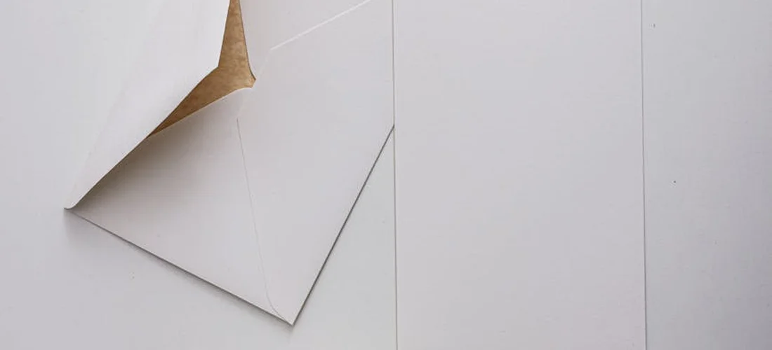Close-up of white folded paper and envelopes on a light surface, symbolizing obituary acknowledgements.
