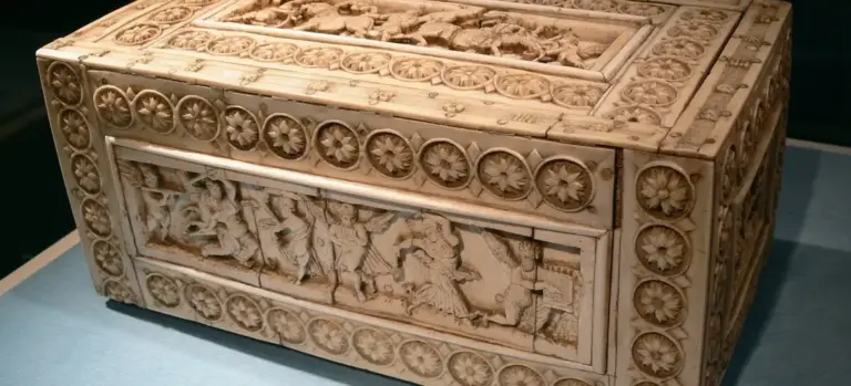 Ornately carved rectangular wooden casket with circular rosette borders and a relief panel on the side, displayed on a blue surface.