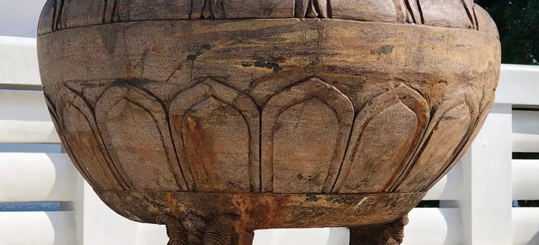 Close-up of an ornate, weathered cremation urn with carved arch-like patterns, set on a pedestal outdoors.