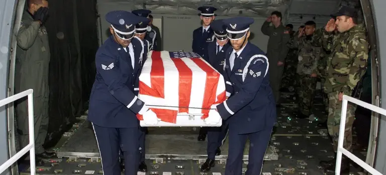A team of uniformed pallbearers carry a flag-draped casket from a military aircraft.