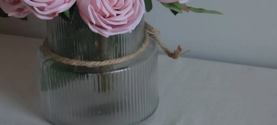 Pink roses in a ribbed glass vase tied with twine on a light surface.
