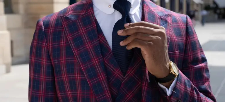 Close-up of a person in a red plaid suit jacket and navy tie, adjusting the tie.