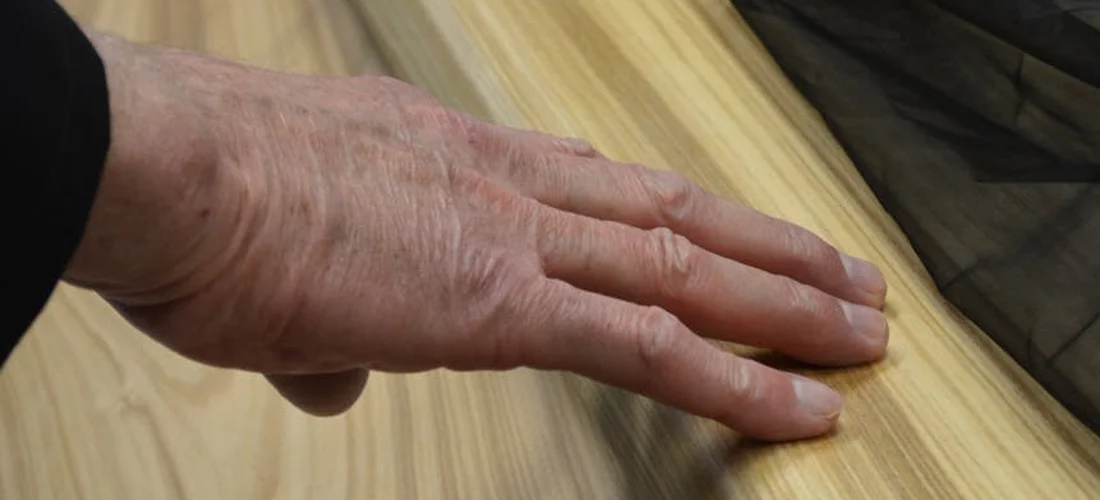 Close-up of a hand resting on a wooden surface with a dark fabric nearby, illustrating the careful, hands-on approach to pressing funeral flowers.