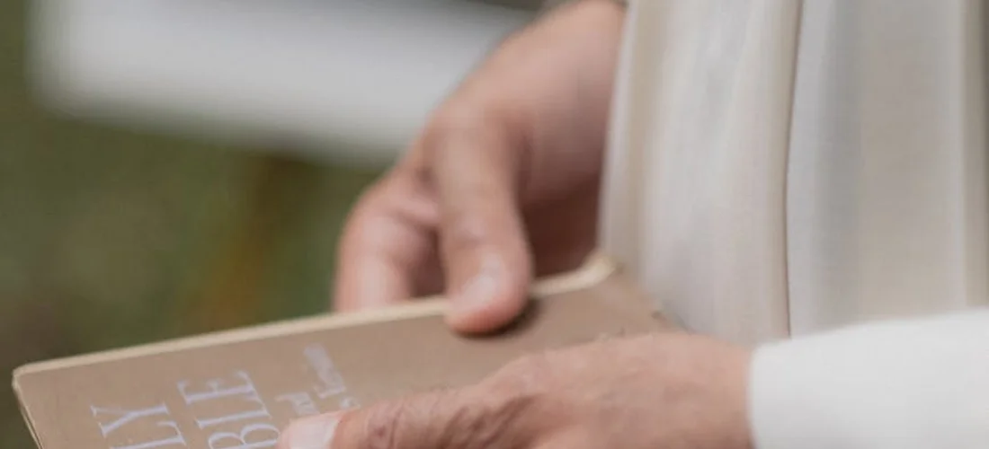 Close-up of hands holding a brown prayer book, symbolizing solemn religious rites.