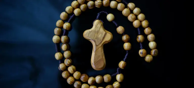 Wooden rosary beads arranged in a loop with a wooden cross pendant on a dark blue background