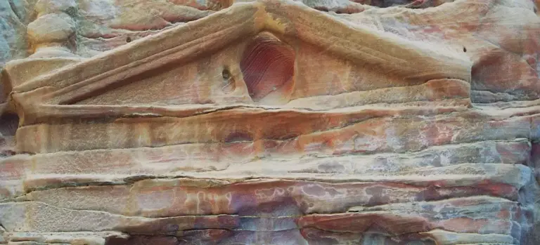 Close-up of a weathered sandstone wall with a decorative arch and circular niche.