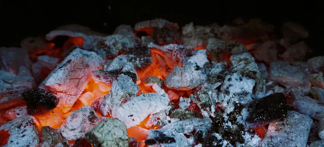 Close-up of cremation remains with glowing orange embers and pale gray-white ash.