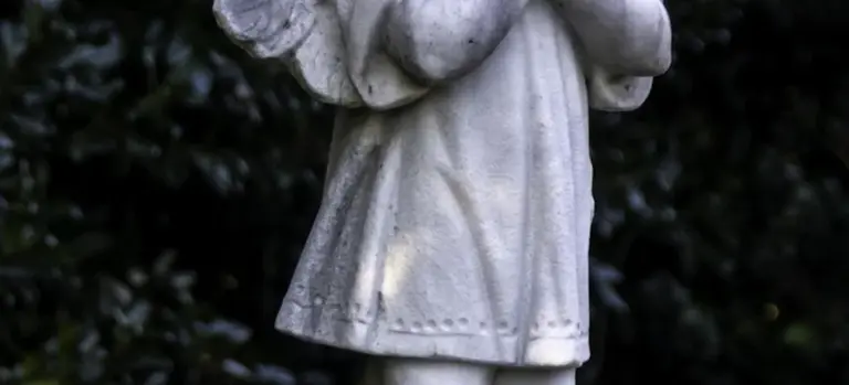 Statue of a child wearing a white robe, shown in a close-up with a dark background
