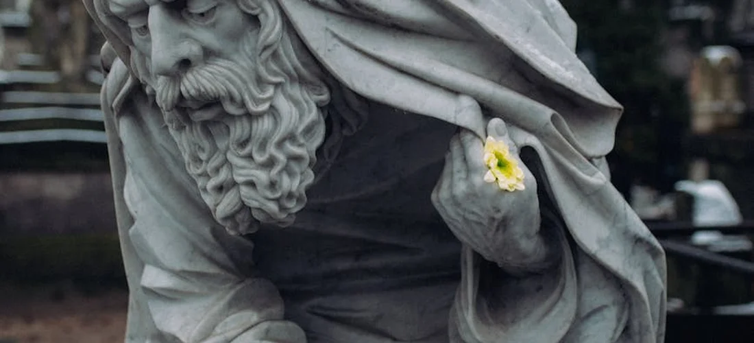 A stone statue with a small yellow flower tucked into its draped garment