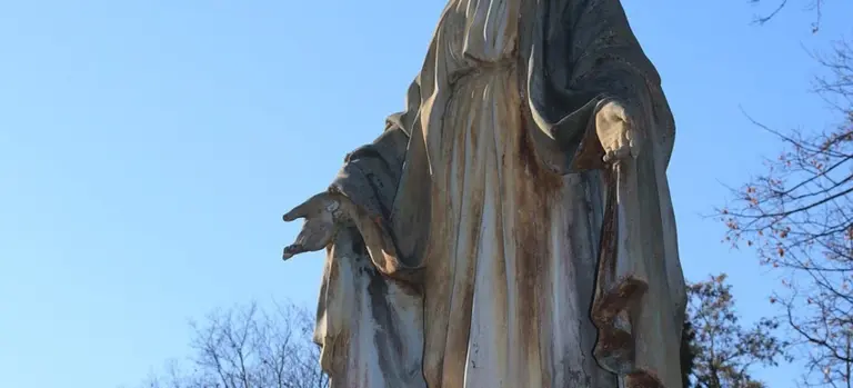 Stone statue of a robed figure outdoors against a clear blue sky