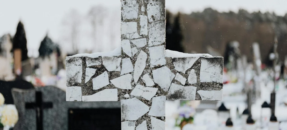 A mosaic stone cross in a cemetery with blurred gravestones in the background.