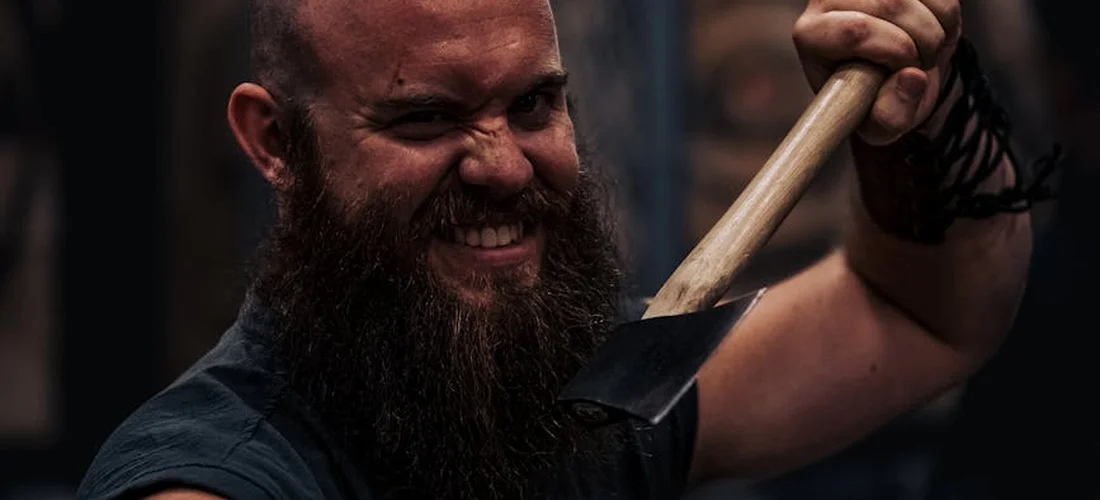 Bearded man gripping a ceremonial axe, smiling as he prepares for a symbolic Viking funeral on land