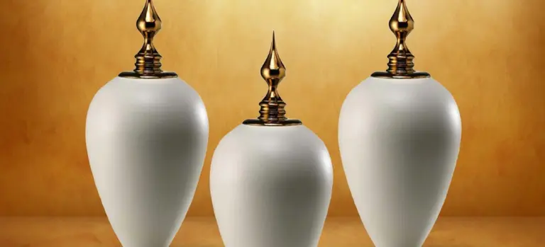 Three white cremation urns with gold-toned caps arranged in a row against a warm golden background.