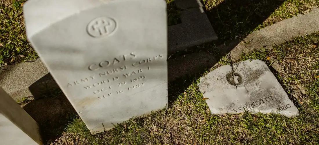 Graveyard scene with a white upright headstone and a small flat marker on grassy ground, illustrating traditional burial.