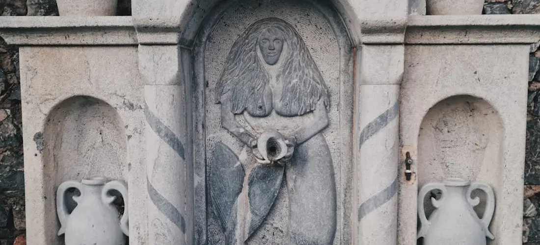 Stone memorial with a central carved figure flanked by two urn-like vases in a cemetery setting
