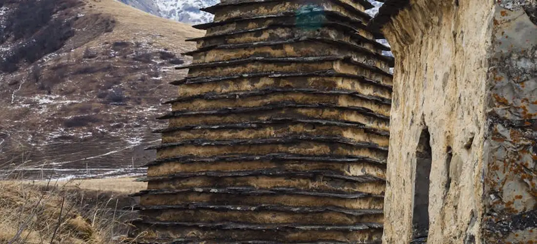 Tiered stone monument beside a rock-cut doorway in a barren landscape.